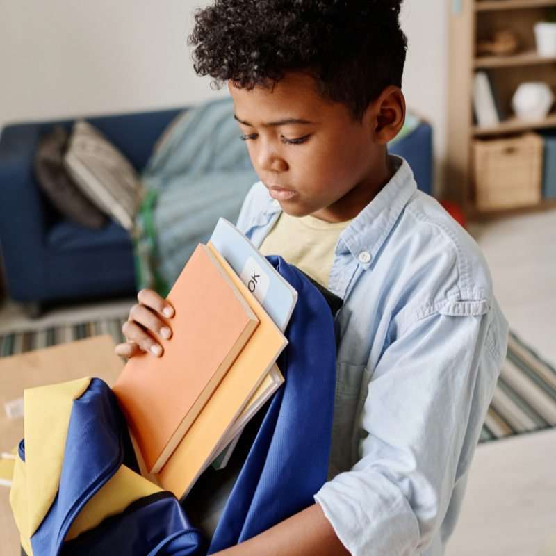 Young boy filling his backpack with folders using supplies from the school supply closet.